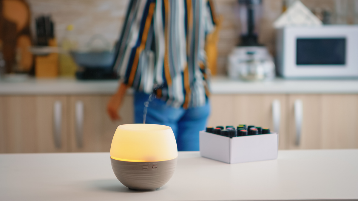 Woman with diffuser on table & essential oil bottles