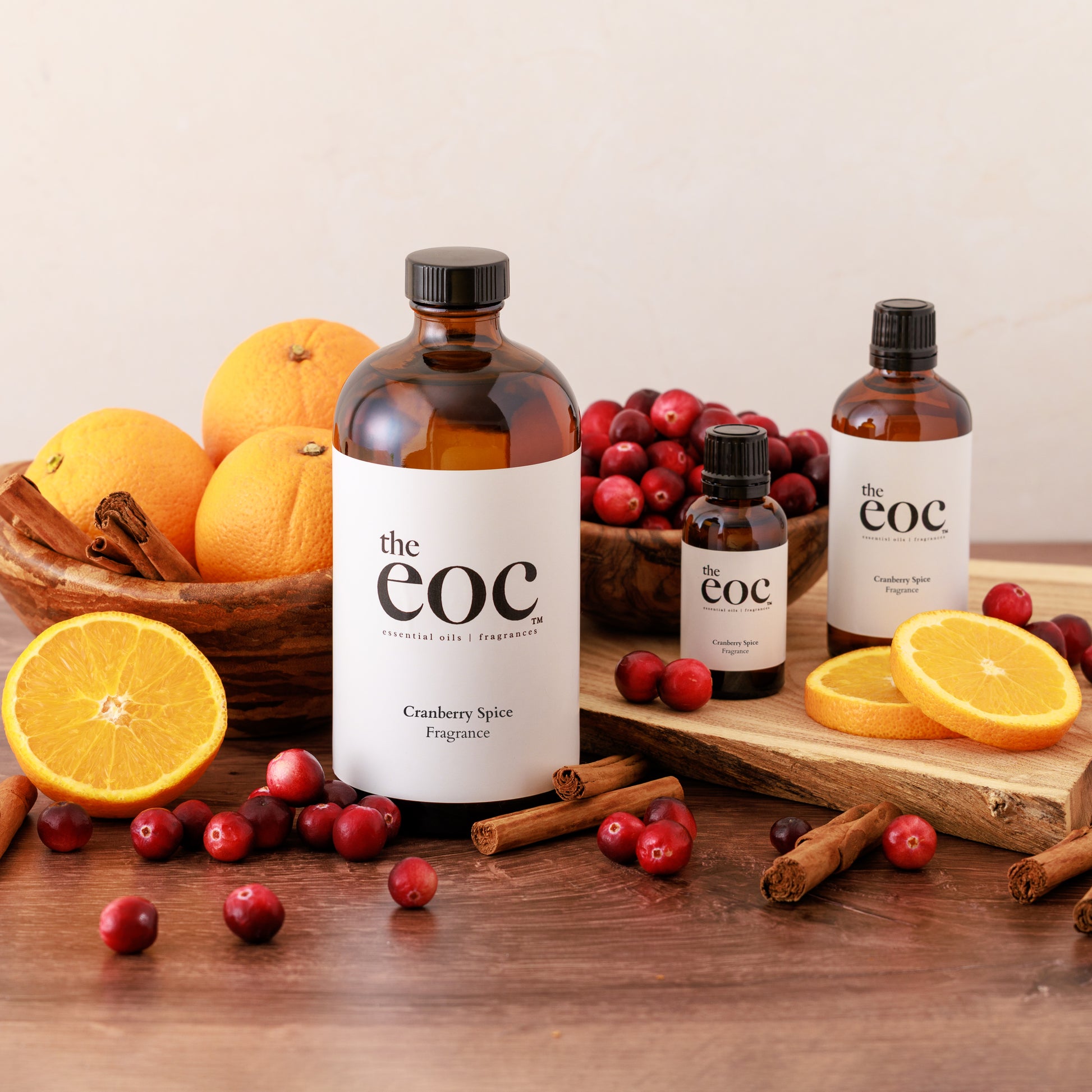 Bottles of 'the eoc' Cranberry Spice Fragrance with oranges, cranberries, and cinnamon on a wooden surface.