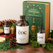 Three bottles of 'the eoc' Dickens' Christmas fragrance with a book titled 'Stories for Christmas by Charles Dickens' on a decorative background.