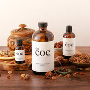 Three bottles of 'the eoc' frankincense and myrrh fragrance on a wooden surface with natural ingredients.