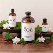 Three bottles of 'the eoc' products on a wooden surface with vanilla beans and orchids.