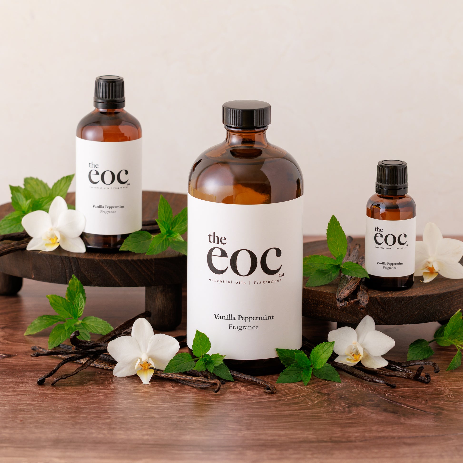 Three bottles of 'the eoc' products on a wooden surface with vanilla beans and orchids.