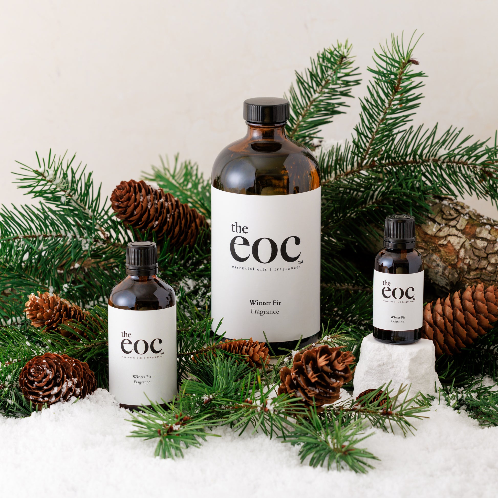 Three bottles of 'the eoc' with labels surrounded by pine branches and pinecones on a snowy background.