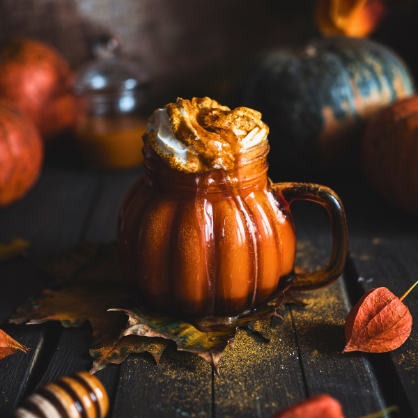 Pumpkin-themed hot chocolate with whipped cream and honeycomb on a wooden surface with pumpkins in the background.