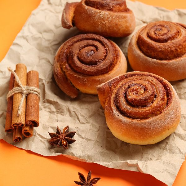 Cinnamon rolls on brown paper with cinnamon sticks and star anise on an orange background
